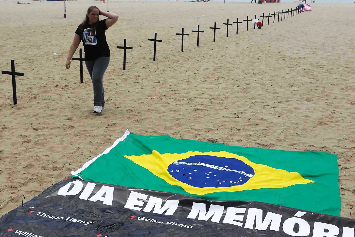 image: A woman walks next to crosses, and a banner reading 'Day of Remembrance' on Copacabana beach, Rio de Janeiro. Brazil, Dec. 15 2012.