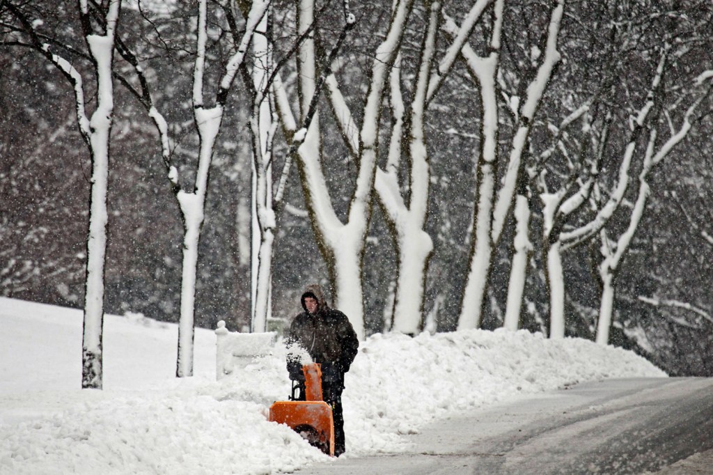 image: Trees covered in snow, added a stark quality to the scene as a man in West Bend, Wis., uses a snowblower to clear away a walkway on Dec. 20, 2012.