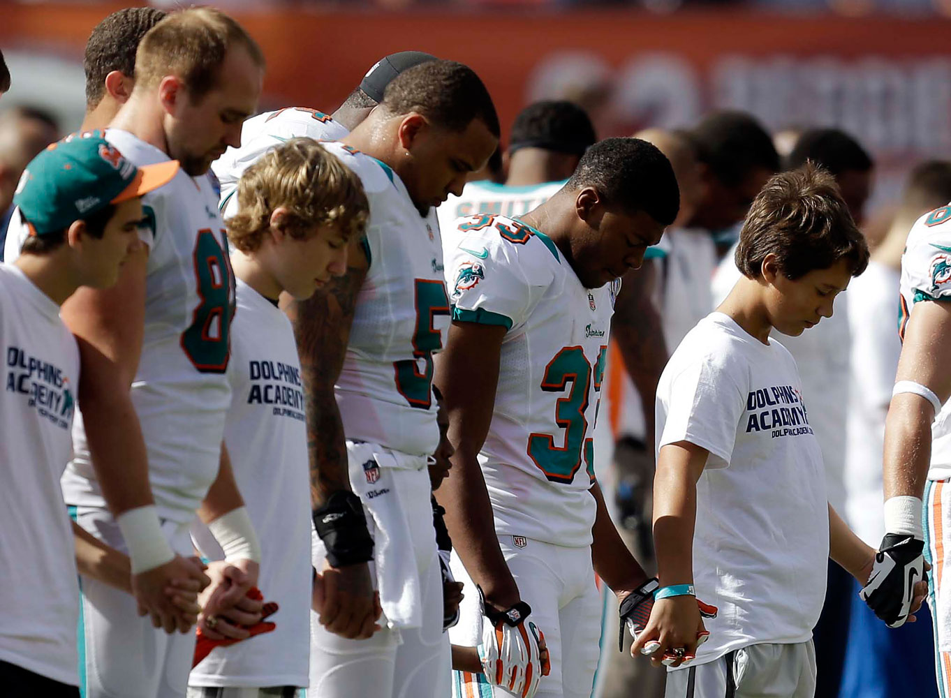 image: Miami Dolphins and young football players hold hands during a moment of silence for the victims of Friday's Sandy Hook Elementary School shootings