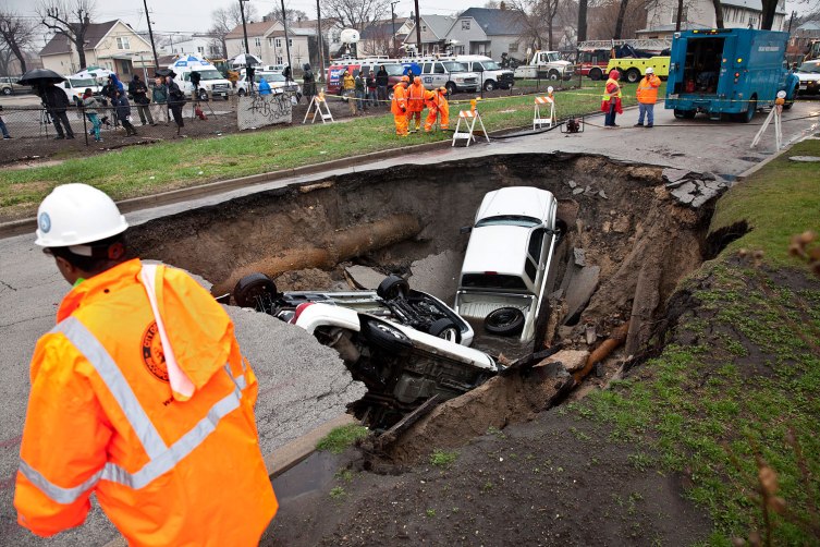 Chicago fire, water, streets and sanitation departments respond to a sink hole which swallowed three vehicles and exposed a 24 inch gas line at the 9600 block of south Houston Avenue on Chicago's south side, April 18, 2013.