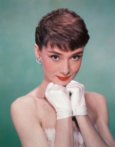 Portrait of Belgian-born American actress Audrey Hepburn as she wears a strapless gown and holds white kid-gloved hands up to her chin, early 1950s.
