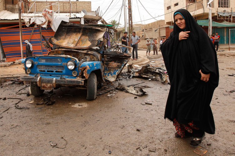 An Iraqi woman passes by the scene of a car bomb attack in the Kamaliyah neighborhood, a predominantly Shiite area of eastern Baghdad, Iraq, Monday, May 20, 2013.