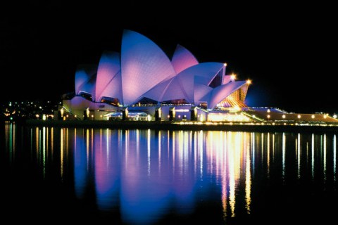 Sydney Opera House lit up at night, reflections in water of harbour