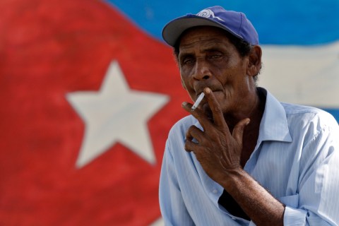 A man smokes a cigarette near a mural with a Cuban flag in Holguin