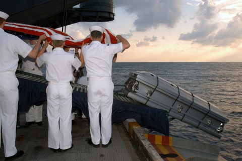 Casket of US Navy Sailor is sent over the edge of aircraft carrier during burial at sea ceremony.
