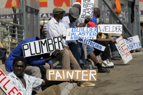 Men hold placards offering temporal employment services in Glenvista, south of Johannesburg