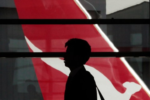 Passenger walks in front of the tail of a Qantas plane at Sydney airport