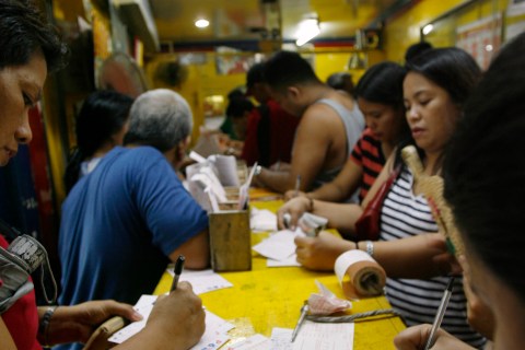Lottery hopefuls fill out lotto tickets in a lottery stall in Manila