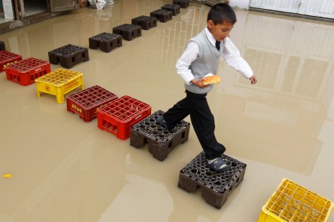 A child, holding a bread, walks on crates on a flooded street in the Bosa neighbourhood in Bogota