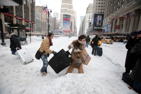 Travellers carry their luggage through a snow bank on 7th Avenue in front of Penn Station after a snow storm in New York
