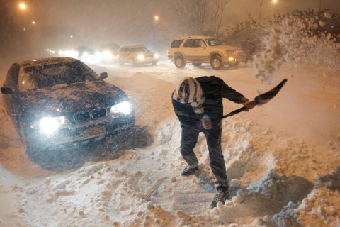 A man tries to dig his car out of the snow while a line of cars behind him waits for an expressway to re-open on Long Island