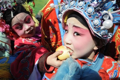 A child performer in traditional costumes eats bread as they rehearse for the upcoming Lantern Festival at a park in Taiyuan