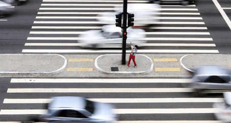 A mime artist gestures to pedestrians across a traffic light red to show them how to cross the road safely at Sao Paulo's Paulista Avenue