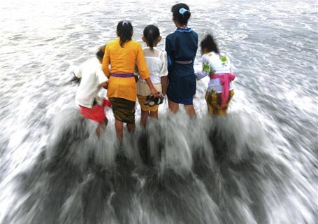 Children play with waves as they attend the Melasti ceremony prayer on a beach in Sanur at Bali