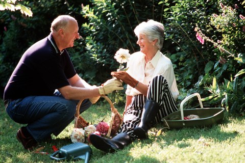Stock Photography: A portrait of a mature couple aged 50-60 years old, both smiling whilst the man presents the lady with a flower from a basket in a sunlit garden.