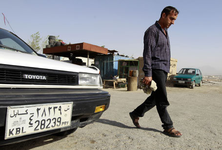A man walks past a car with the number "39" on its license plate in Kabul