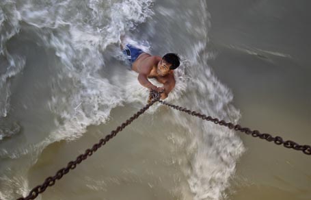 A man clings to chains suspended from a bridge as he bathes in rapidly flowing waters of the Ganges river in Haridwar