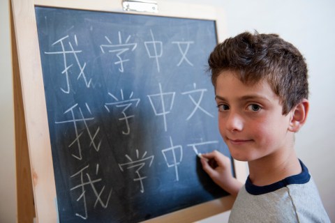 Young boy writing mandarin Chinese on blackboard
