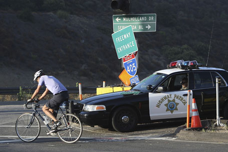 A cyclist passes a California Highway Patrol officer at the 405 onramp from Skirball Center Drive during the demolition of the Mulholland Drive bridge across the 405 freeway in Los Angeles, California.