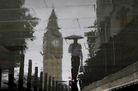 A man is reflected next to Big Ben on a wet pavement during a rainy day in central London