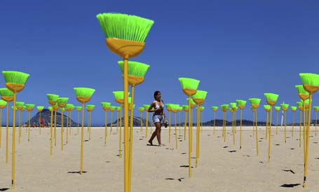 A woman walks near brooms placed at Copacabana beach as a form of protest in Rio de Janeiro