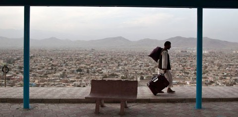 A man carries a bag over his shoulder as he pulls a suitcase in Kabul