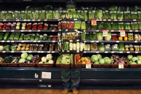 Artist Liu Bolin demonstrates an art installation by blending in with vegetables displayed on the shelves at a supermarket in Beijing