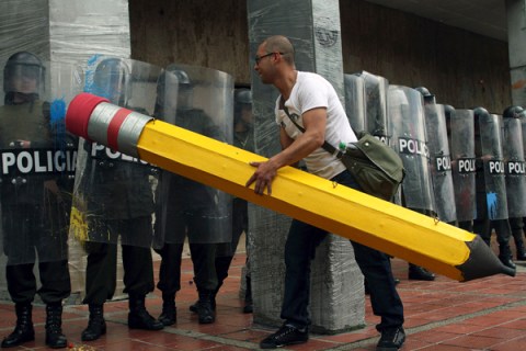 A student holding a pencil tries to 'erase' riot police during a demonstration in Bogota