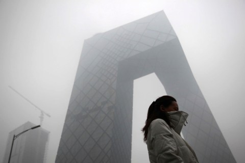 A woman walks past the new China Central Television building amid heavy fog in Beijing