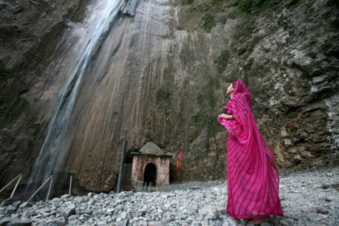 A woman watches a waterfall after performing prayers at the temple of Baba Dhansal at Reasi