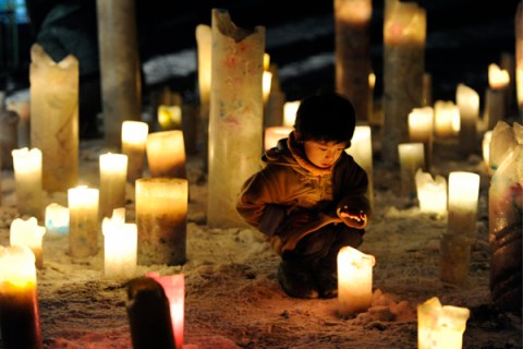 Child looks at candle flame during event to pray for reconstruction of areas devastated by March 2011 quake and tsunami, in Iwanuma
