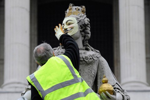 An official removes a mask placed on a statue of Britain's Queen Anne at the 'Occupy' camp outside of St Paul's Cathedral in London