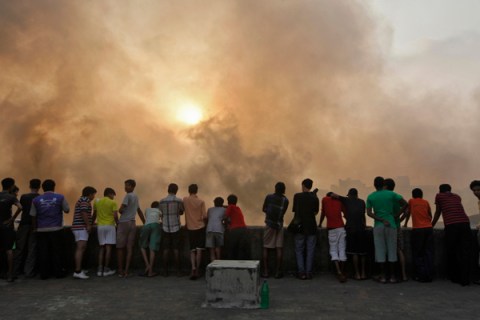 Onlookers stand atop a building amid smoke rising from a burnt market in Kolkata