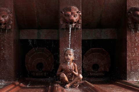 A boy cools himself off as he sits under a fountain in New Delhi