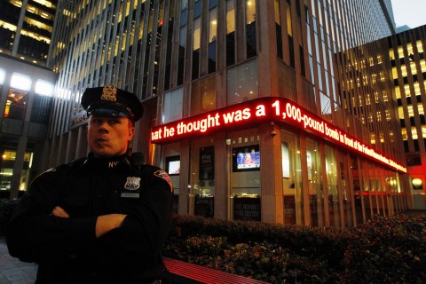 NYPD officer stands in front of a news ticker mentioning arrest of Bangladeshi man during a sting operation in New York