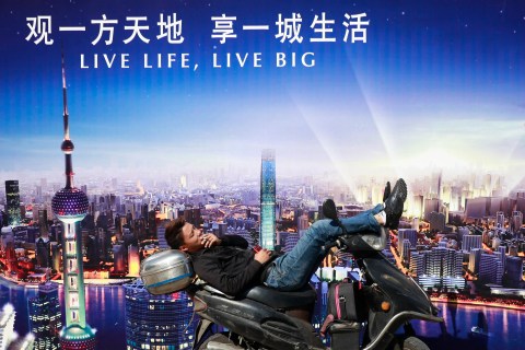 Man rests on a motorcycle in front of an advertisement in central Shanghai