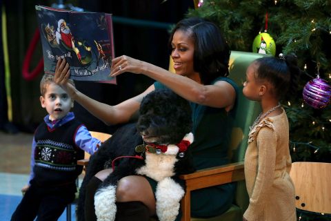 images: First Lady Michelle Obama reads a Christmas story while her dog Bo sits on her lap at Children's National Medical Center on December 14, 2012 in Washington, DC.