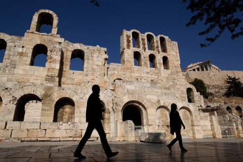 Tourists walk in front of the ancient Herodes Atticus theatre below the hill of the Acropolis in Athens