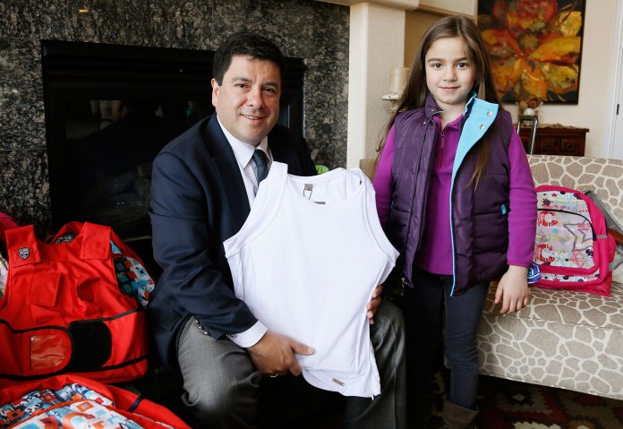 Miguel Caballero, CEO of the Miguel Caballero Company holds an armored tank top as he poses with Lana wearing a MC Kids Ballistic Puffer Vest both sold by Elite Sterling Security LLC in Aurora