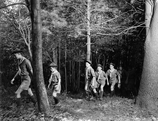 Boy scouts hiking through the woods with their group leader, circa 1940.