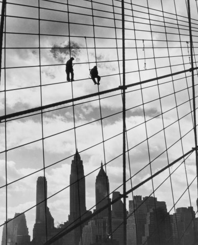 Two workers climb the suspension cables of the Brooklyn Bridge, above the Empire State Building and the Manhattan skyline, circa 1930.