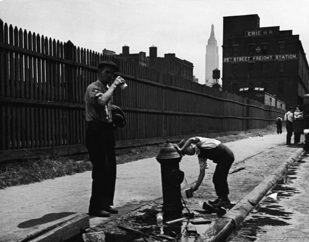 A man and a young boy drink from an open fire hydrant near the 28th Street Freight Station, just South of the Empire State Building in New York City, circa 1930s.