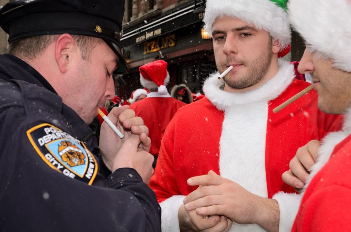 A police officer smokes a cigarette with SantaCon participants on Second Avenue.