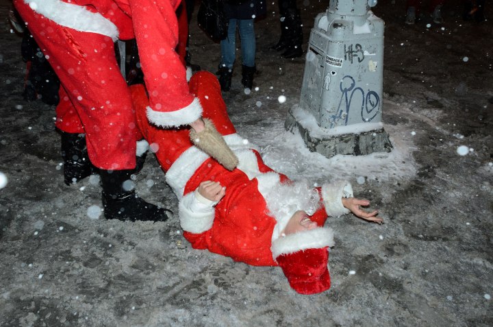 A SantaCon participant lends a helping hand to a fellow Santa after he slipped on the ice on Second Ave.